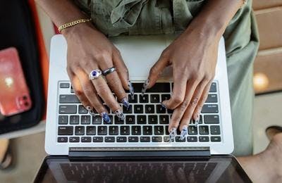 A woman, having long nails, typing something on her laptop