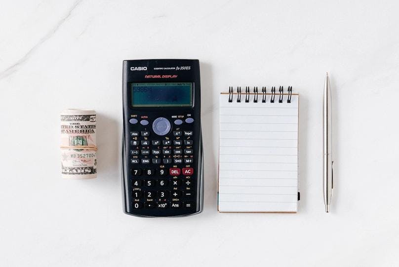 A calculator, a pen, a notepad, and money on the table